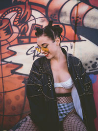 Young woman sitting against graffiti on wall