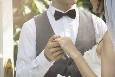 Midsection of bride and groom holding hands at wedding