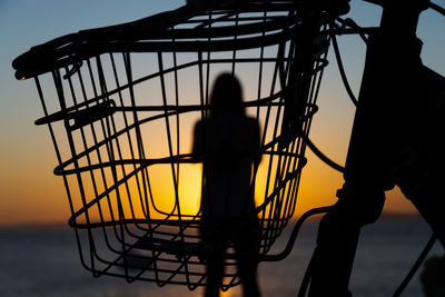 Low angle view of silhouette woman standing by sea against sky during sunset