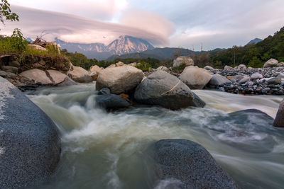 Rocks in river by mountains against sky