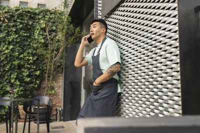 Surprised man talking through mobile phone leaning on wall