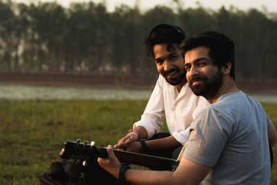 Portrait of smiling men with guitar against trees