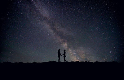 Silhouette man and woman standing on field against star field