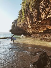 Man on rocks at beach against sky