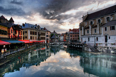 Canal amidst buildings in city against sky at sunset