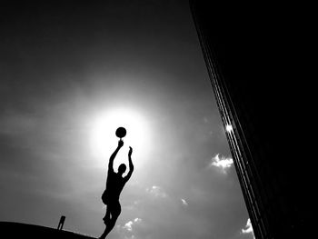 Low angle view of silhouette man playing with ball against sky