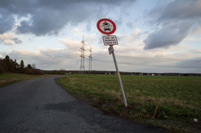 Road sign on field against sky