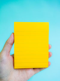 Close-up of yellow hand holding paper against blue background