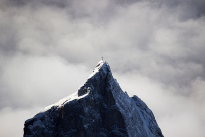 Dramatic view of mountain peak with summit cross in front of stormy clouds