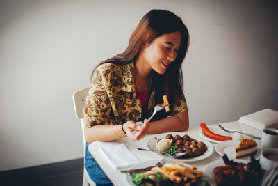 Young woman looking away while sitting on table against wall