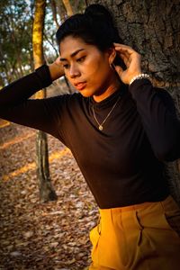 Young woman looking away while standing on tree