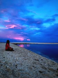 Rear view of woman sitting on rock by sea against sky