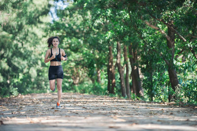 Full length of determined young woman jogging on road amidst trees