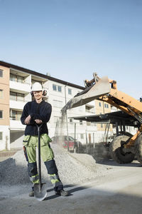 Full length portrait of confident construction worker with shovel standing at site