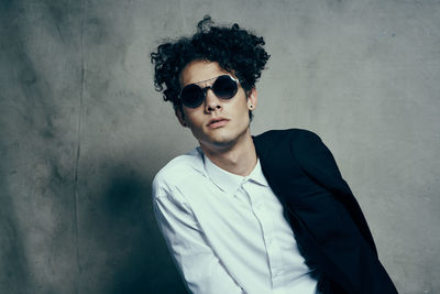 Portrait of young man wearing sunglasses standing against wall