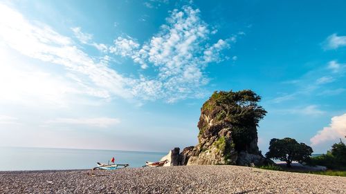 People sitting on rock by sea against sky