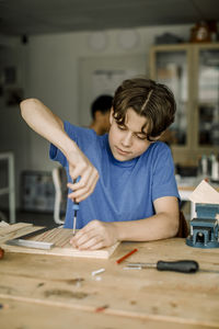 Male teenage student working with screwdriver during carpentry class at high school