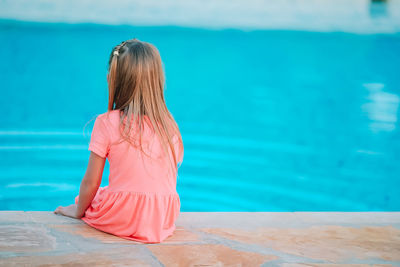 Rear view of view of girl sitting by swimming pool