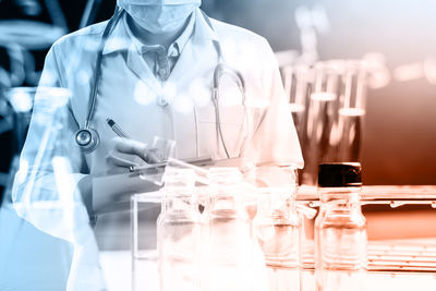 Double exposure of female doctor writing on clipboard with chemicals in laboratory