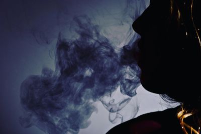 Close-up of silhouette woman smoking against gray background