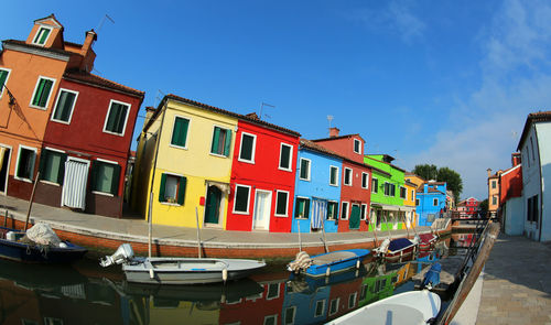 Boats moored in canal by buildings against blue sky