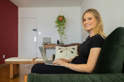 Woman working at home from couch with laptop on her lap. home office concept. gray notebook