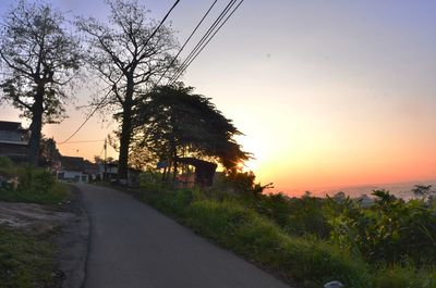 Road amidst trees against sky during sunset