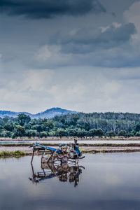 Abandoned tractor on wet agricultural field against cloudy sky