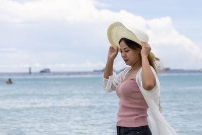 Young woman standing at beach against sky