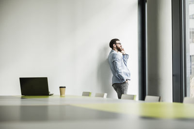 Young businessman standing in office, using smart phone