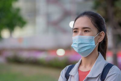 Young woman wearing mask looking away while standing outdoors