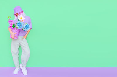 Full length of woman holding flowers standing against aqua background
