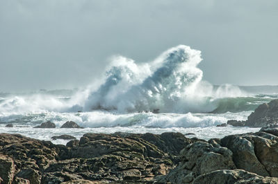 Panoramic view of waves breaking on rocks against sky