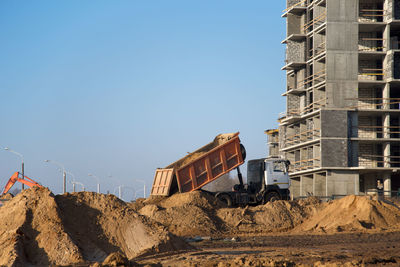 Construction site by buildings against clear blue sky