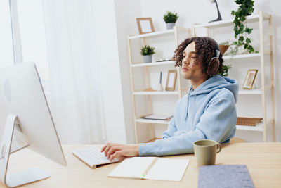 Young woman wearing wireless headphones using desktop pc at home