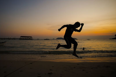 Silhouette man jumping on beach against sky during sunset