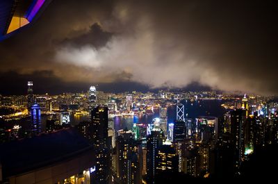 High angle view of illuminated cityscape against cloudy sky at night