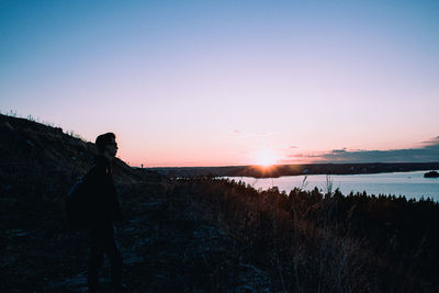 Side view of silhouette man standing on landscape against sky during sunset