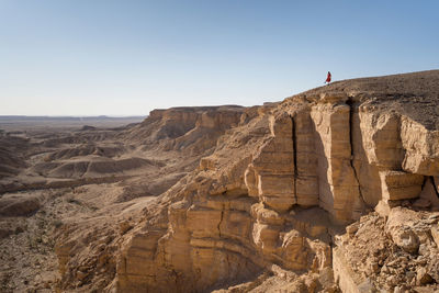 Side view of anonymous woman in casual clothes sitting on cliff in the edge of the world in saudi arabia