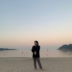 Woman standing on beach against sky during sunset