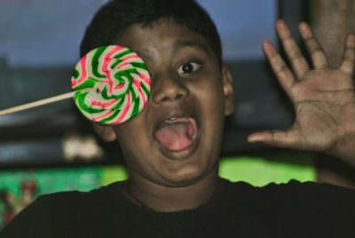 Portrait of shocked boy covering eye with lollipop