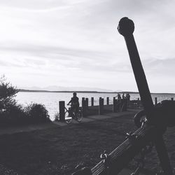 Man on bicycle by sea against sky