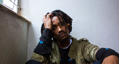 Portrait of young man with head in hands sitting against wall