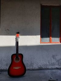 Guitar propped by a wall next to a window