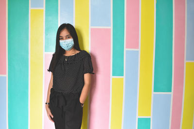 Full length portrait of young woman standing against wall