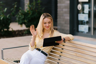 Stylish woman is sitting on a bench in the summer and talking on a tablet via video link