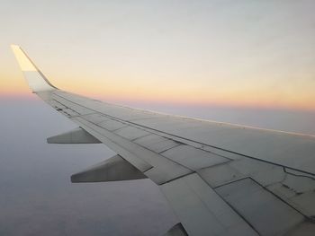 Close-up of airplane wing against sky during sunset