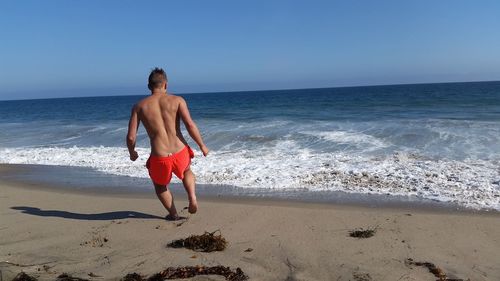 Rear view of shirtless man running at beach