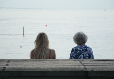Rear view of grandmother sitting with granddaughter by sea