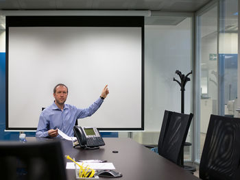 Portrait of businessman sitting by projection screen in board room at office